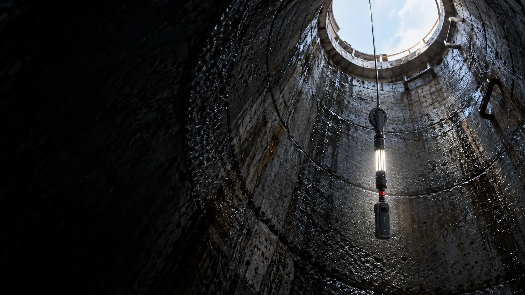 Illustration of a slim panoramic camera suspended below a vertical LED light inside a concrete manhole.