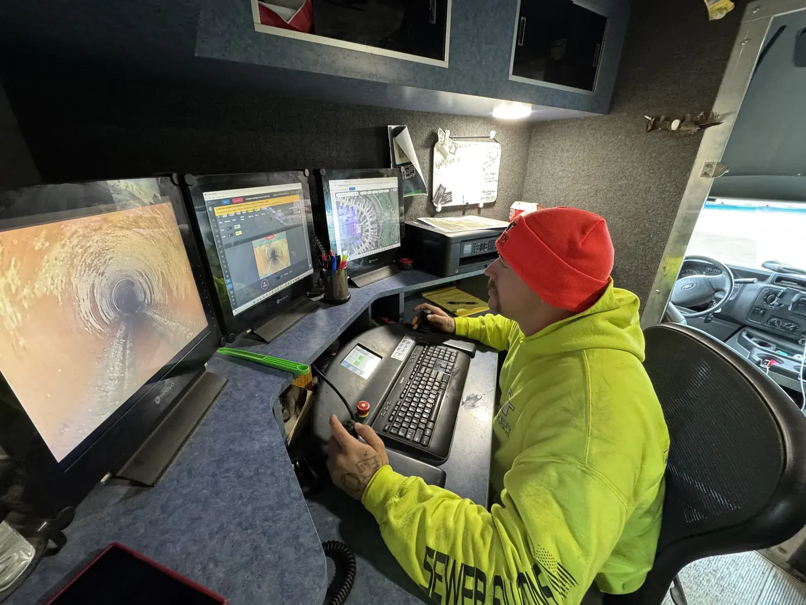 A CIT operator reviews live sewer inspection video at the control console inside a televising truck.