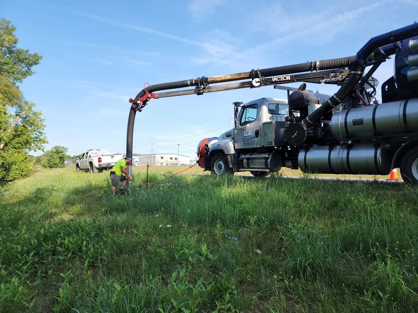 A CIT vacuum truck working from a grass shoulder with its boom extended over the work area.