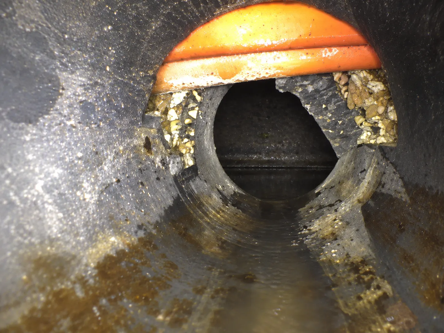 Recreated inspection-camera view showing an orange utility near the top of a damaged sewer lateral opening.
