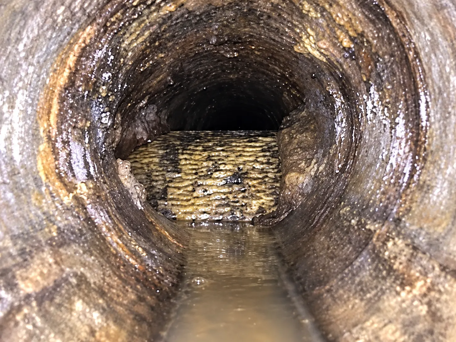 Recreated inspection-camera view showing a wide textured obstruction across the lower part of a sewer opening, with water below.
