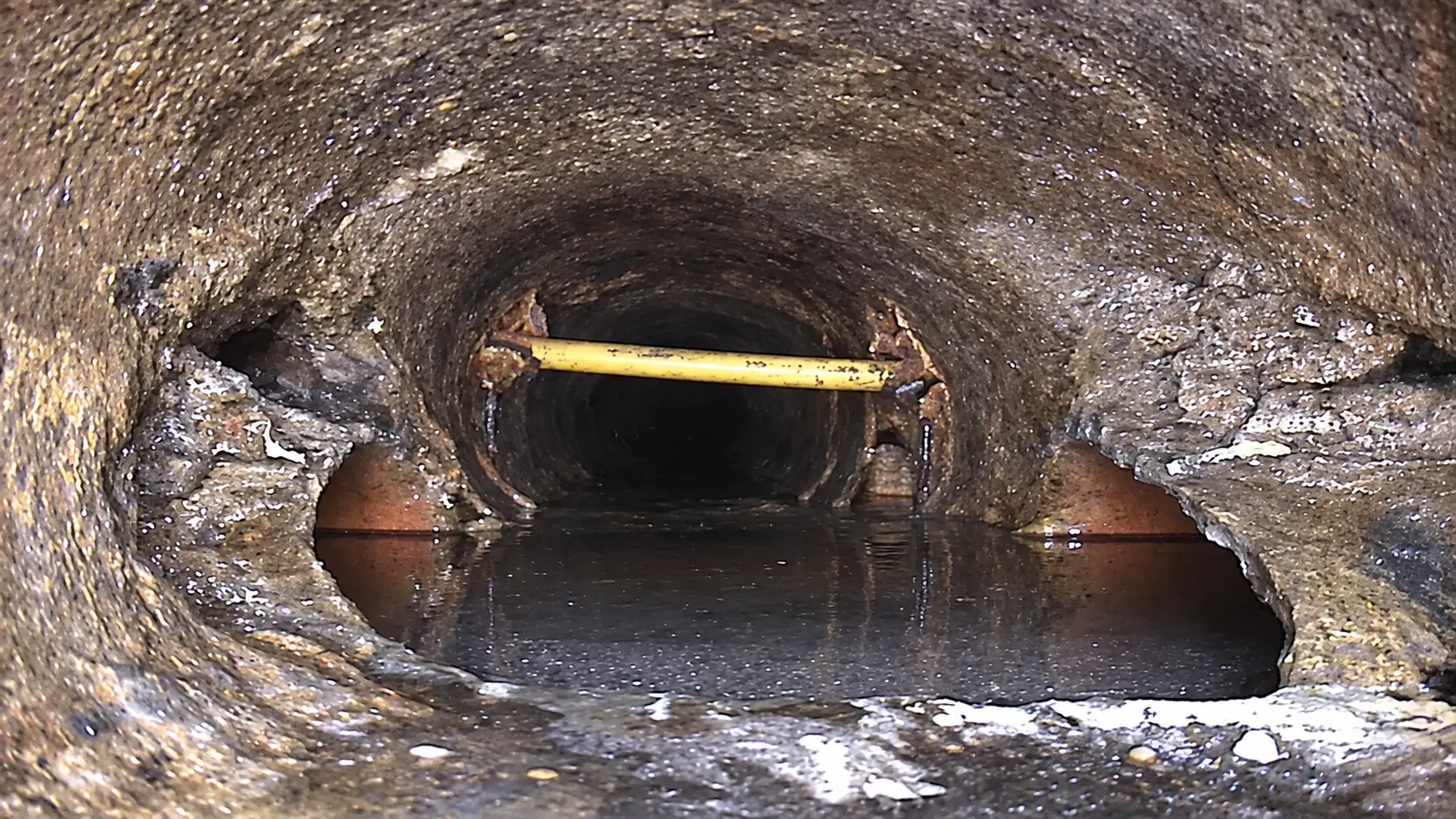 Realistic service illustration of a yellow utility crossing a sewer opening, recreated from the original inspection view without instrument overlays.