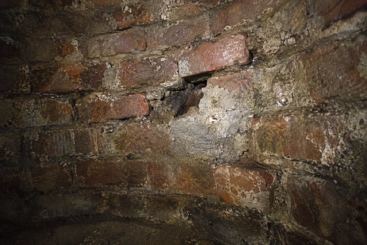 Condition illustration of an aging brick manhole with missing mortar, displaced bricks and old patch repairs.