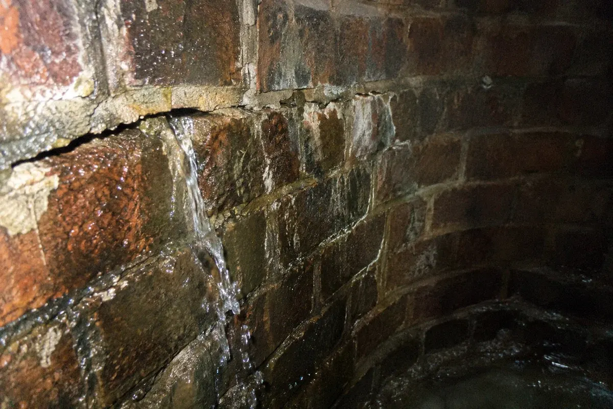 Condition illustration of water streaming from an open joint in a brick manhole wall.