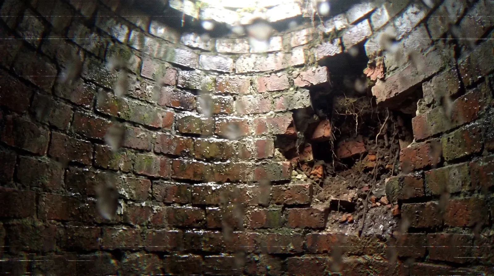 Wide view of deteriorated brickwork and a large opening through a manhole wall.